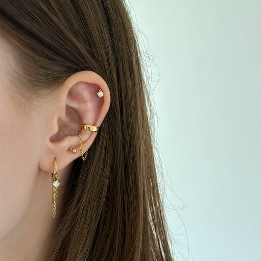 Composition avec une mono boucle d'oreille dorée pendante avec chaîne et strass en acier inoxydable et un faux piercing pour le conch doré