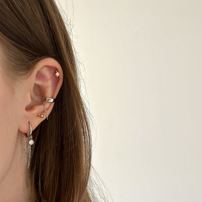 Composition avec une mono boucle d'oreille dorée pendante avec chaîne et strass en acier inoxydable et un faux piercing pour le conch argenté