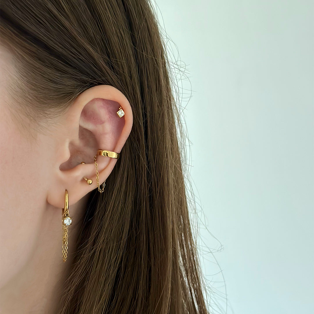 Composition avec une mono boucle d'oreille dorée pendante avec chaîne et strass en acier inoxydable et un faux piercing pour le conch doré